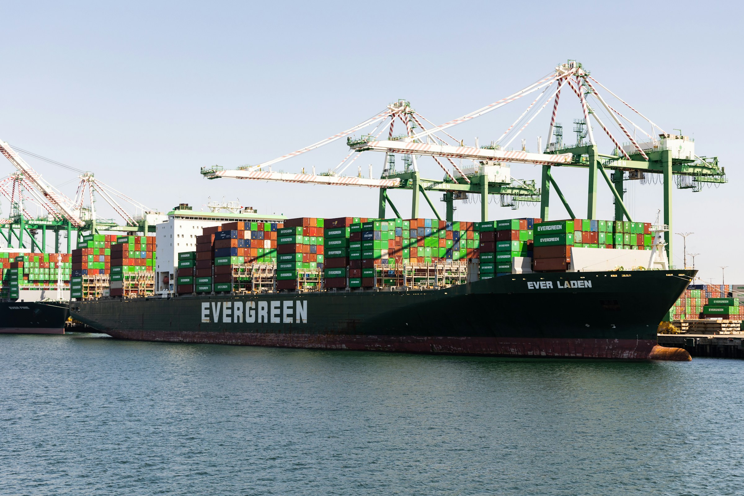 A container ship alongside green port cranes.