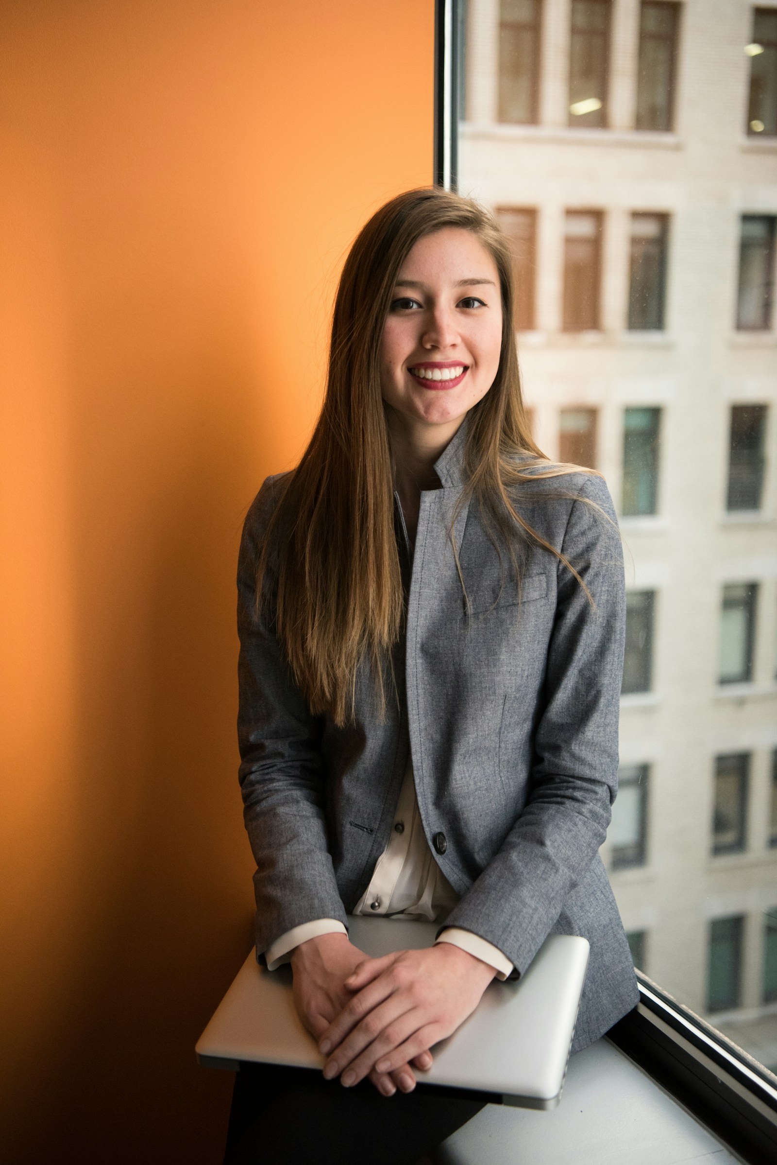 A woman wearing glasses and a gray blazer stands in an office.